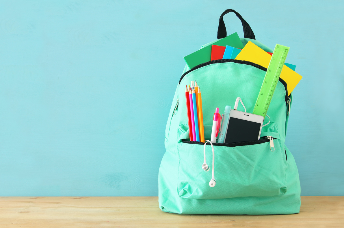 school bag with stationery and notebooks in front of wooden blue background. Back to school concept.
